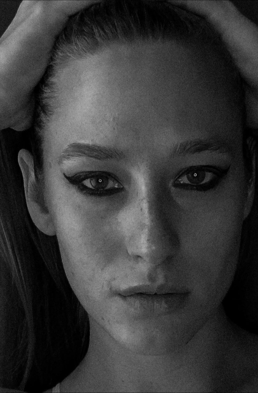 Black-and-white close-up portrait of Dasha looking straight at the camera, hands in her hair